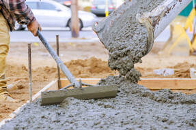 Worker using rake to level out wet cement being pumped from a concrete truck into a formed footing.