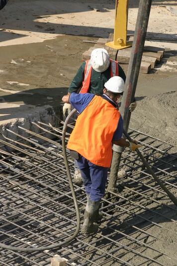 Two workers using a pump truck pumping concrete into a commercial concrete foundation construction site. 